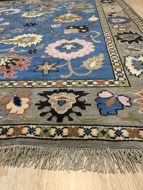 Traditional blue and gray floral patterned rug with long fringe rests on light wood flooring.