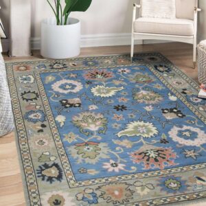 Floral blue and grey area rug centered on wood flooring near a white armchair and large planter.