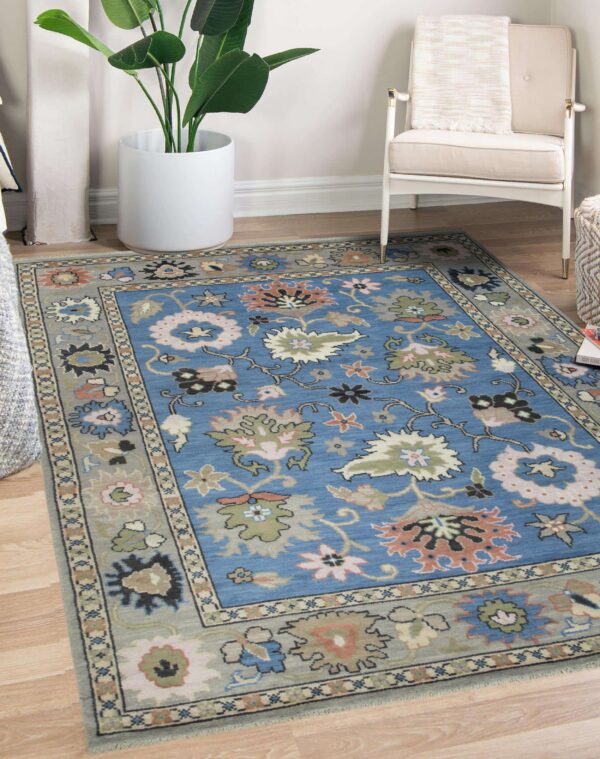 Floral blue and grey area rug centered on wood flooring near a white armchair and large planter.
