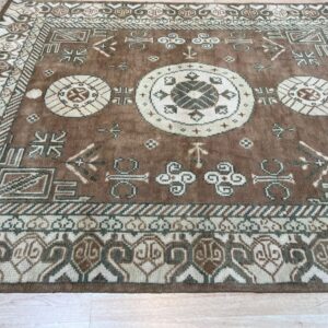 Brown geometric rug with cream and olive medallions and borders resting on light wood plank flooring.