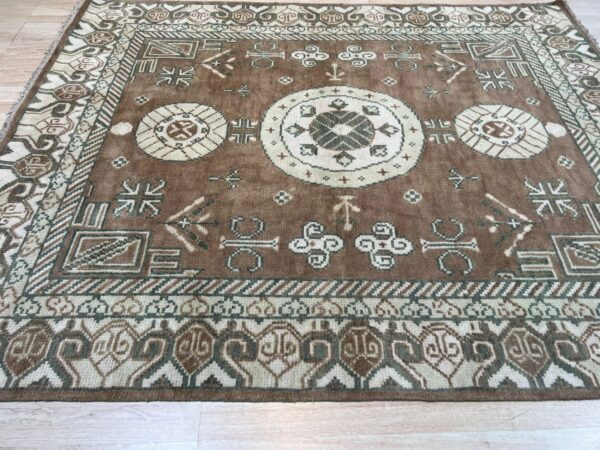 Brown geometric rug with cream and olive medallions and borders resting on light wood plank flooring.