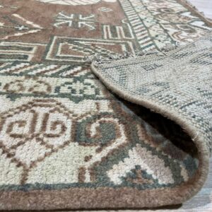 High-pile rug in brown, cream, and green tribal patterns, folded over on light wood flooring.