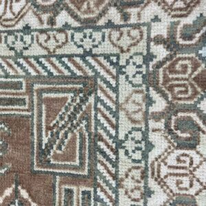 Detailed close-up of a textured rug featuring complex geometric patterns in brown, off-white, and muted green.
