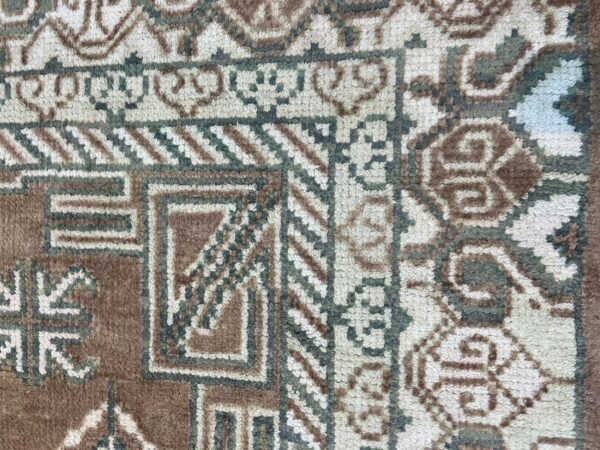 Detailed close-up of a textured rug featuring complex geometric patterns in brown, off-white, and muted green.