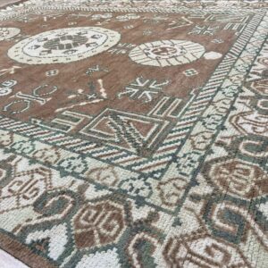 Textured high-pile rug in brown, cream, and green with a dense, traditional tribal pattern on wood flooring.