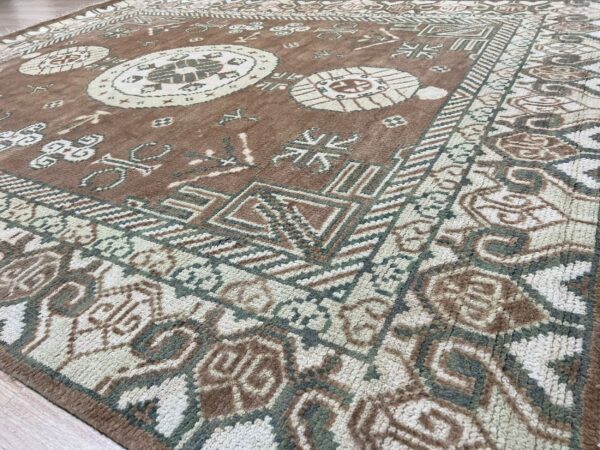 Textured high-pile rug in brown, cream, and green with a dense, traditional tribal pattern on wood flooring.
