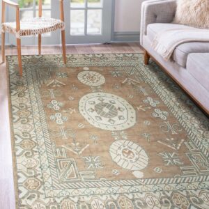 Traditional tan, cream, and green geometric rug placed beneath a wooden chair and a light gray sofa.