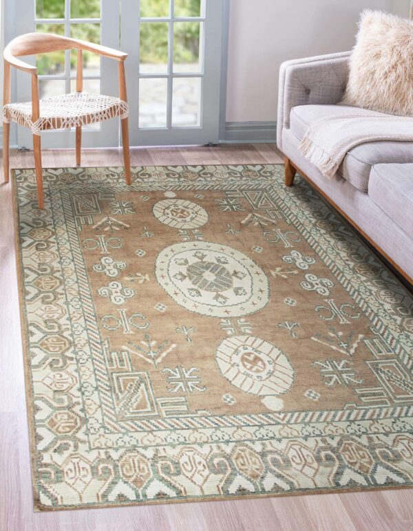 Traditional tan, cream, and green geometric rug placed beneath a wooden chair and a light gray sofa.
