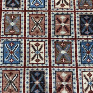 Repeating grid pattern rug featuring geometric motifs in navy, bright blue, red, brown, and cream colors.