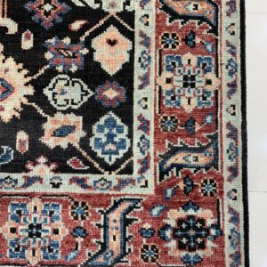 Textured high-pile rug corner featuring black, terracotta, blue, and pale pink traditional geometric patterns on white flooring.