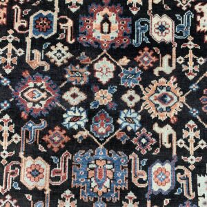 Detailed low-pile rug surface with a dark field and dense motifs in cream, blue, red, and peach.