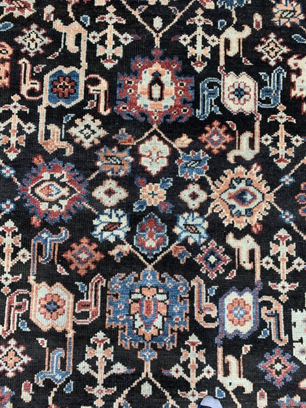 Detailed low-pile rug surface with a dark field and dense motifs in cream, blue, red, and peach.