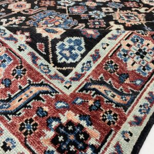 Close-up of a high-pile rug with black, red, blue, and peach traditional geometric patterns.