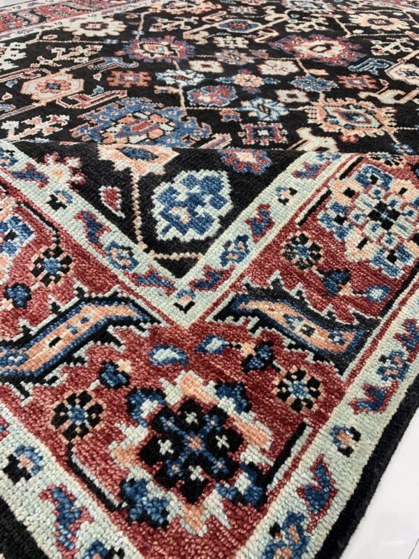 Close-up of a high-pile rug with black, red, blue, and peach traditional geometric patterns.