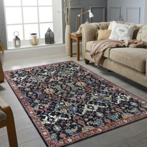 Dark blue traditional rug featuring red and teal motifs on gray wood plank flooring by a beige sofa.
