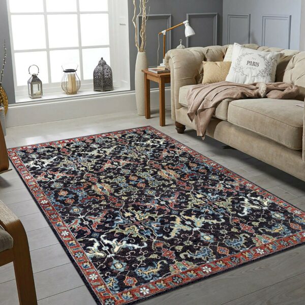 Dark blue traditional rug featuring red and teal motifs on gray wood plank flooring by a beige sofa.