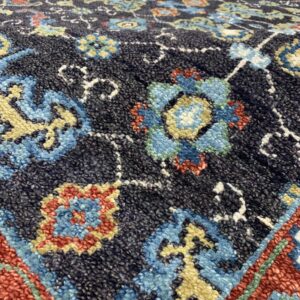 Textured high-angle detail of a rug showing a dark background with blue, red, and yellow floral designs.