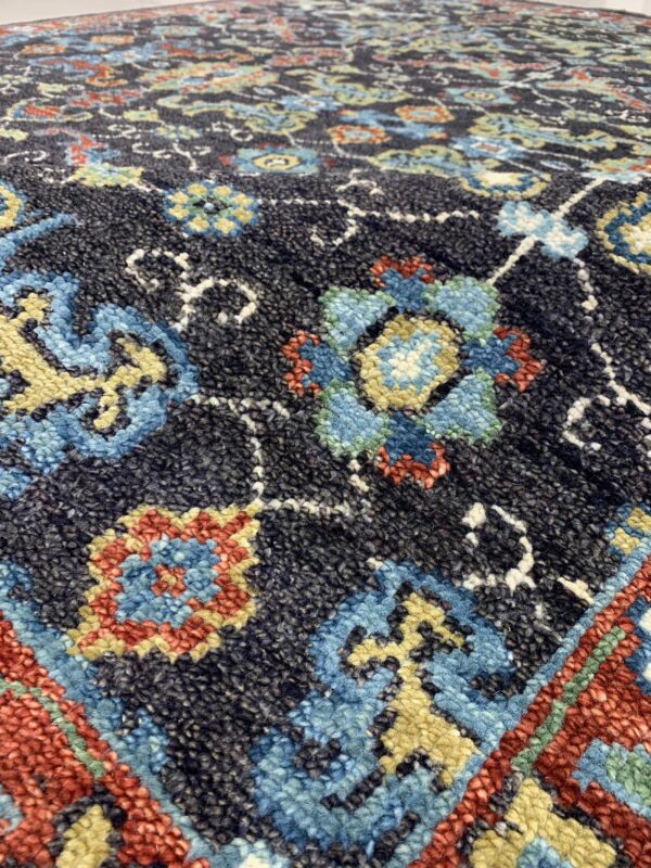 Textured high-angle detail of a rug showing a dark background with blue, red, and yellow floral designs.