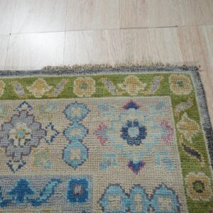 Textured rug displaying blue, green, and cream floral patterns rests upon light, wood-look plank flooring.