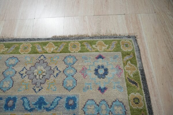 Textured rug displaying blue, green, and cream floral patterns rests upon light, wood-look plank flooring.