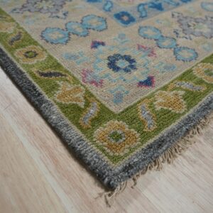 Multi-colored traditional rug with a textured green border and fringe resting on light wood flooring.