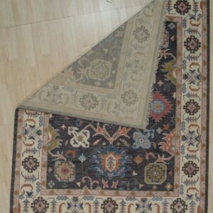 Dark gray traditional rug with floral motifs, folded back to display the lighter reverse side on wood flooring.