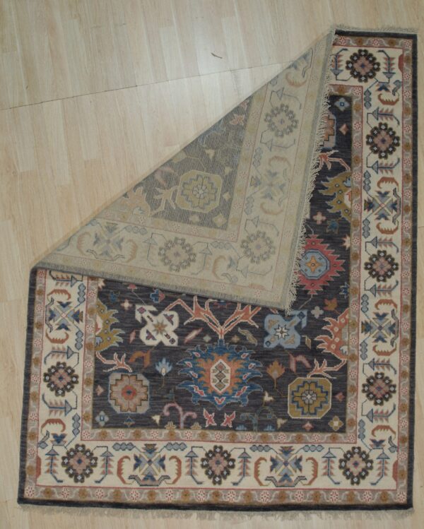 Dark gray traditional rug with floral motifs, folded back to display the lighter reverse side on wood flooring.