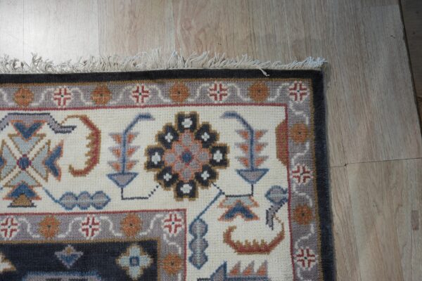 Geometric and stylized rug with blue, gray, and orange motifs on a cream field and light wood floor.