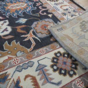 The edge of a dark patterned rug with cream and gray motifs is folded back on light wood flooring.
