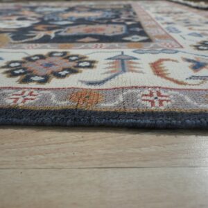 Low-angle view of a patterned rug border in cream, navy, and rust resting on light wood floors.