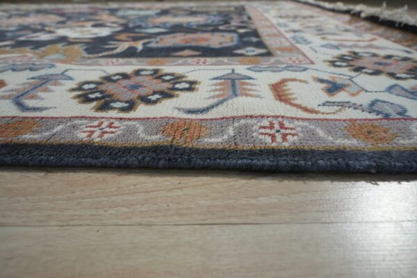 Low-angle view of a patterned rug border in cream, navy, and rust resting on light wood floors.
