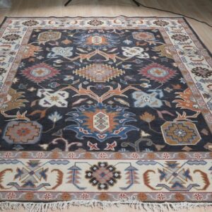 A dark charcoal and cream traditional rug featuring multicolor floral motifs displayed on light wood flooring.