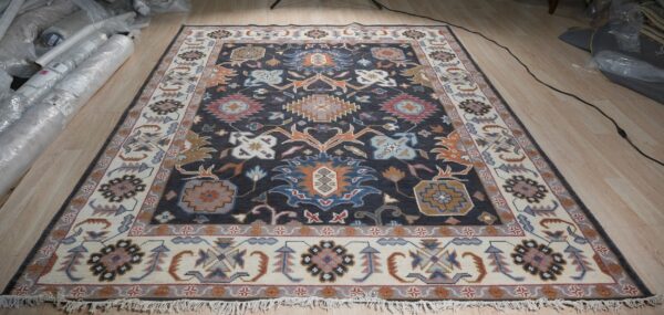 A dark charcoal and cream traditional rug featuring multicolor floral motifs displayed on light wood flooring.
