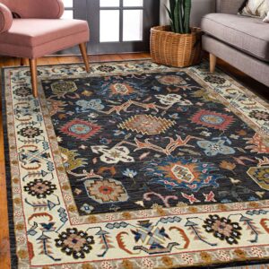 Colorful geometric patterned rug with a dark field and cream border sits between a pink chair and grey sofa.