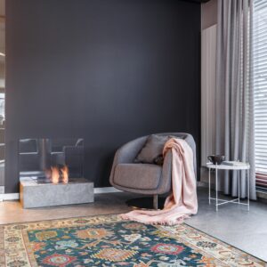 Teal, rust, and gold patterned rug anchors a modern gray room with a fireplace and armchair.