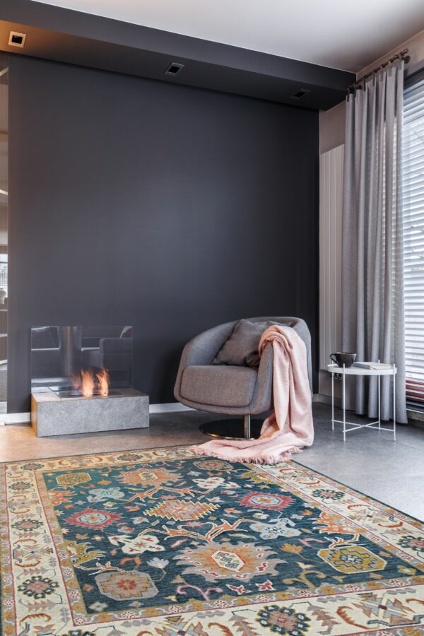 Teal, rust, and gold patterned rug anchors a modern gray room with a fireplace and armchair.