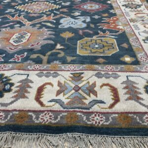 Medium-pile rug featuring a deep blue field and ivory border with multicolored tribal designs resting on light wood floors.