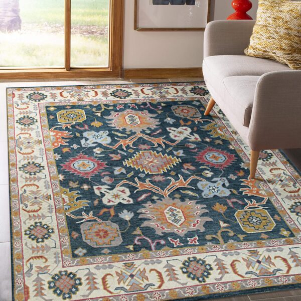 Colorful traditional patterned rug, navy blue field, wide cream border, next to a gray sofa and large window.
