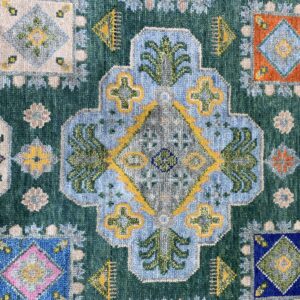 Teal rug featuring multicolored traditional geometric designs, including a large blue medallion and scattered square motifs.