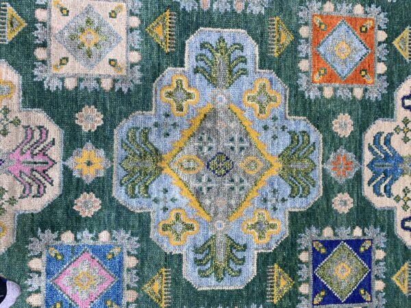 Teal rug featuring multicolored traditional geometric designs, including a large blue medallion and scattered square motifs.