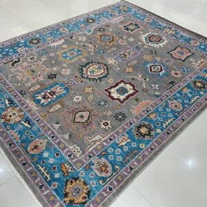 Gray low-pile rug with colorful tribal motifs and turquoise and lavender borders on reflective white tile.
