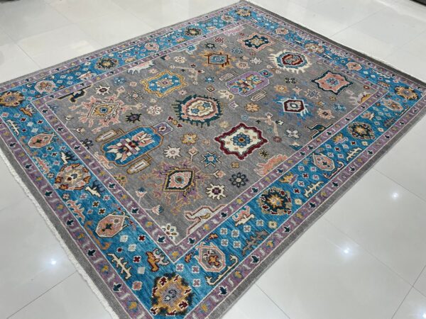 Gray low-pile rug with colorful tribal motifs and turquoise and lavender borders on reflective white tile.