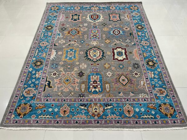 A gray rug featuring colorful geometric medallions and a prominent turquoise and lavender multi-layered border.