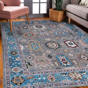 A traditional gray rug with multicolored geometric patterns rests between a pink chair and a gray sofa.