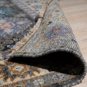 Close-up shows a rolled gray and lavender patterned rug with fringe on light wood flooring.