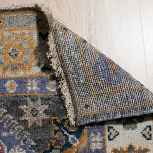 Patterned rug in blue, grey, and gold hues is folded back, showing the backing on light wood floors.