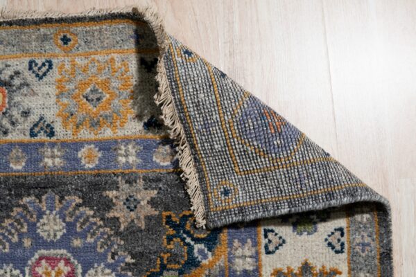 Patterned rug in blue, grey, and gold hues is folded back, showing the backing on light wood floors.