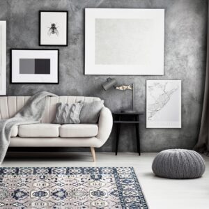 A navy and grey traditional patterned rug sits on light flooring under a cream sofa and textured dark wall.