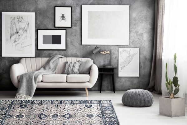 A navy and grey traditional patterned rug sits on light flooring under a cream sofa and textured dark wall.