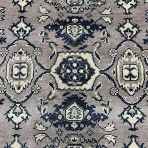 Low-pile rug detail showing a traditional medallion pattern in navy, cream, and medium grey on a mauve field.